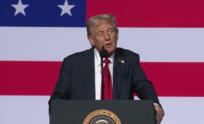 Donald Trump stands behind a lectern before a large American Flag dislay